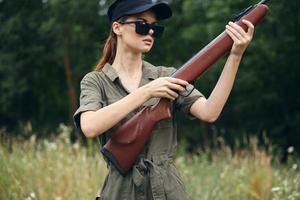 Woman on nature Holds a weapon in his hands, sunglasses, green overalls black cap photo