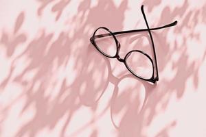 Eyeglasses on pink background with flower shadows and copy space photo