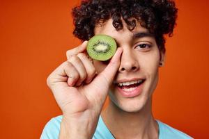 Cheerful guy with curly hair kiwi near the eyes fruit close-up photo