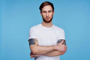 handsome man in white t-shirt tattoos on his arms cropped view blue background photo
