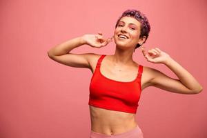 Fashion portrait of a woman with a short haircut of purple color and a smile with teeth in a red top on a pink background happiness photo