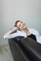 mujer acostado a hogar en el sofá retrato con un corto Corte de pelo en un blanco camisa, sonrisa, depresión en adolescentes, hogar fiesta foto