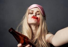 borracho mujer con un botella de cerveza en un gris antecedentes gestos con su manos y brillante maquillaje foto
