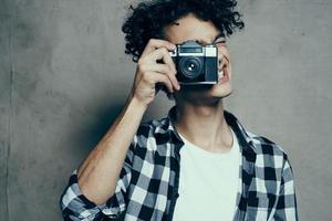 fotógrafo en un tartán camisa con un cámara en su mano en un gris antecedentes en un pasatiempo estudio habitación foto