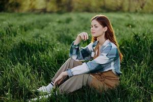 A young beautiful woman sits on the green grass in the park and looks out into the setting sun photo