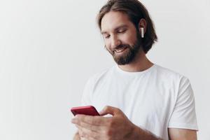 Man blogger holds a phone in his hands and communicates with people online in social networks with a smile and a white t-shirt on a white background photo