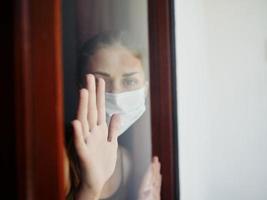 enmascarado mujer mirando fuera el ventana de cerca prohibición foto