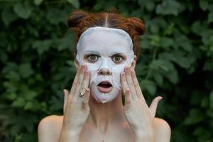 Beautiful woman anti-aging mask Surprised to touch your face with your hands bare shoulders bushes in the background photo