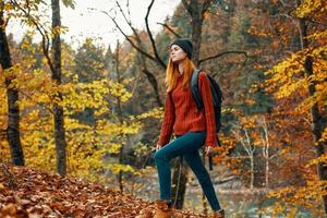 contento mujer caminante con un mochila en su espalda en pantalones y un rojo suéter en el otoño bosque parque paisaje foto