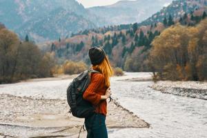 woman in sweater with a backpack rest in the mountains near the river in autumn in nature and tall trees model photo