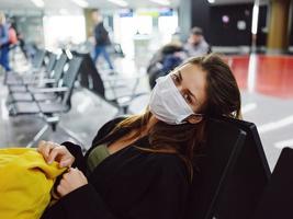 cansado mujer en médico máscara esperando para vuelo aeropuerto foto