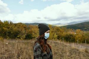 mujer caminante en calentar gorra con un médico máscara en su cara en el bosque foto