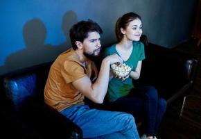 amigos hombre y mujer acecho televisión en el sofá y palomitas de maiz en un plato foto