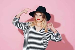 atractivo mujer en negro sombrero y a rayas camisa brillante maquillaje rosado antecedentes foto