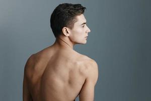 Rear view of a sexy man with a naked back looks to the side on a gray background photo