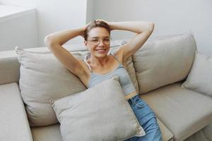 A woman wearing eyeglasses sits on a couch and looks at the camera. Vision problems photo