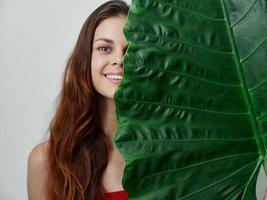 pretty red-haired woman covers half of the leaf with green palm leaf close-up photo