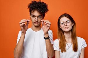 Rizado chico y un niña en blanco camisetas son en pie siguiente a cada otro en un naranja antecedentes foto