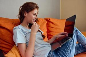 alegre mujer chateando en el naranja sofá con un ordenador portátil estilo de vida foto