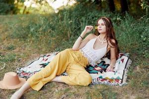 joven hermosa hippie mujer acostado en el suelo en naturaleza en el otoño en eco ropa en amarillo pantalones en el puesta de sol ligero foto