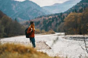 young traveler with a backpack in jeans and a sweater near the river in the mountains photo