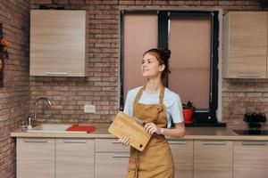 hermosa mujer en un delantal corte tablero con cuchillo en el cocina tareas del hogar casa concepto foto