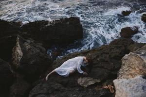 Beautiful bride in a secluded spot on a wild rocky coast in a white dress view from above photo