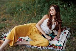 joven hermosa hippie mujer acostado en el suelo en naturaleza en el otoño en eco ropa en amarillo pantalones en el puesta de sol ligero foto