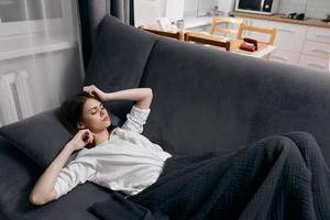 a woman in a white t-shirt lies on the sofa under a blanket and gestures with her hands photo