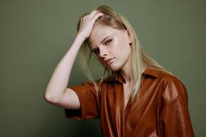 Fashionable stylish woman touching hair posing isolated in brown palette leather dress trench coat isolated on over olive green wall background. Cool offer for brands photo