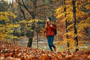 mujer turista camina mediante el parque en otoño con un mochila en su espalda y alto arboles paisaje río lago foto