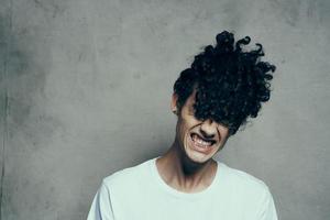 alegre chico con Rizado pelo se inclina su cabeza a el lado en un gris antecedentes estudio fotográfico modelo foto