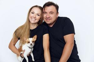 cheerful married couple hugs black t-shirts studio small dog in hands photo