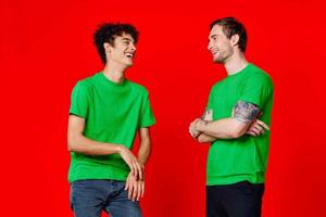 Two cheerful friends in green t-shirts communicating emotions red background photo