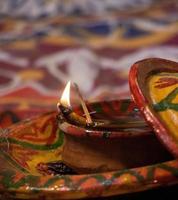 Beautifully decorated clay lamp with a little flame closeup. Traditional Hindu ritual elements. A burning clay lamp close-up with decorated plate, at a Hindu wedding. Hindu religion and Diwali concept photo