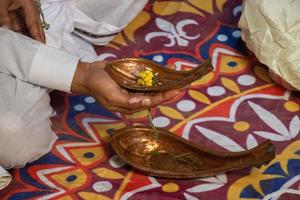 A man groom holding a metal Kosha Kushi in his hand. A decorated copper yoni Hindu prayer elements close-up photo. Decorated Hindu wedding concept with a male groom's hand and metal Kosha Kushi. photo