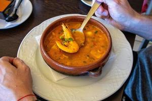 large clay pot with fish soup and shrimp kept on a spoon photo