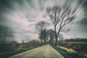 old narrow asphalt road with trees on the side of the road during a car ride in early spring photo