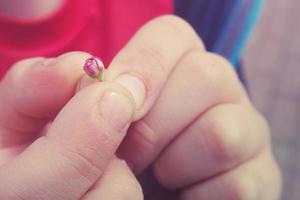 pequeño delicado blanco-rosa flor mantenido en el dedos de un pequeño niño mano foto
