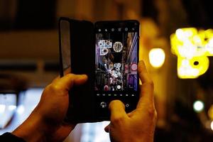 del hombre manos con un móvil teléfono tomando imágenes de el Navidad calle a noche foto