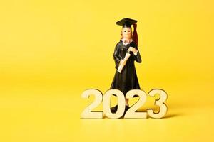 Class of 2023 concept. Wooden number 2023 with graduate statuette on color background photo