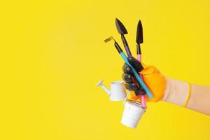 A hand in a glove holds gardening tools on a yellow background. Gardening concept photo