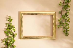 Empty golden frame with green twigs on a beige background. Spring mock up flat lay, top view. photo