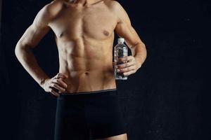 a man with a pumped up press in black shorts gym dark background photo