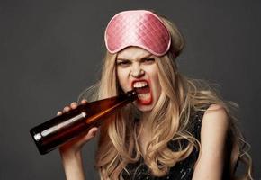 Angry woman with a bottle of beer in her hand with bright makeup and a pink sleep mask photo