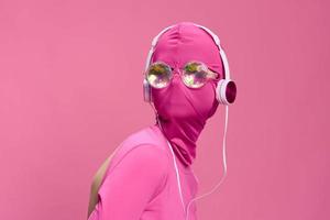 Creative fan art photo of a young female cyberpunk blogger on a pink background wearing a pink full-face mask with glowing round glasses and headphones