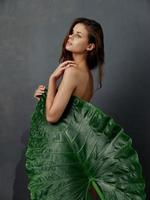 charming woman with green leaf covers naked body dark background photo