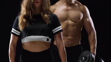 Athletic man and woman doing exercise on the shoulders with elastic bands on a black background in studio video