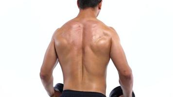 Man flexes his hands with dumbbells, training his shoulders on a white background in the studio video