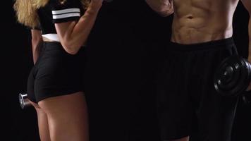 athlétique homme et femme Faire exercice sur le épaules avec élastique bandes sur une noir Contexte dans studio video